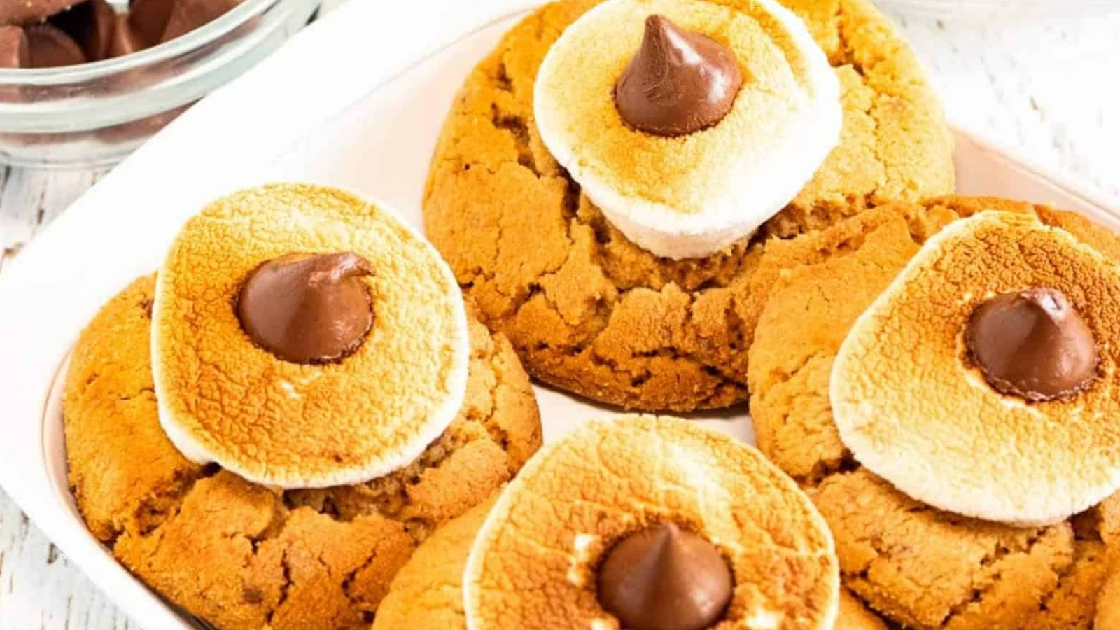 Cookies topped with toasted marshmallows and chocolate drops on a white plate.