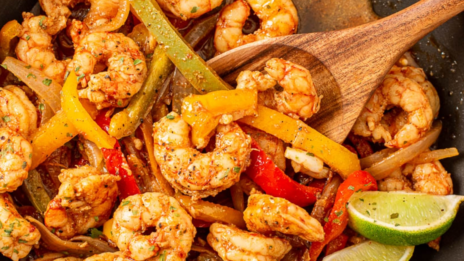 Shrimp and peppers in a skillet with serving spoon.