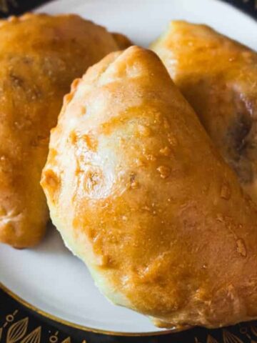 Three golden-brown empanadas on a decorative black and gold plate.