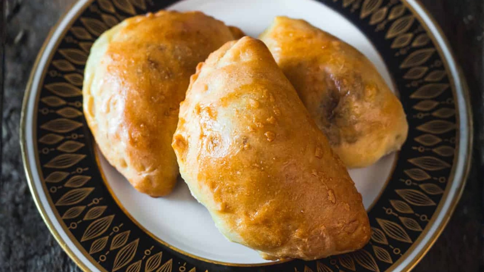 Three golden-brown empanadas on a decorative black and gold plate.
