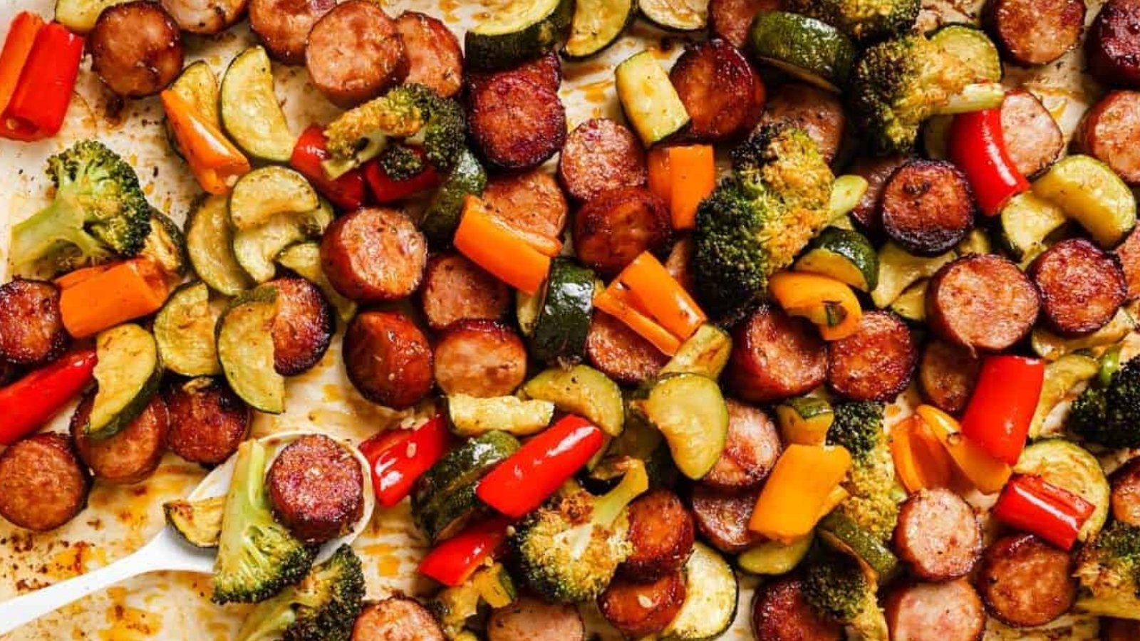 Sausage and veggies sheet pan dinner with a spoon.