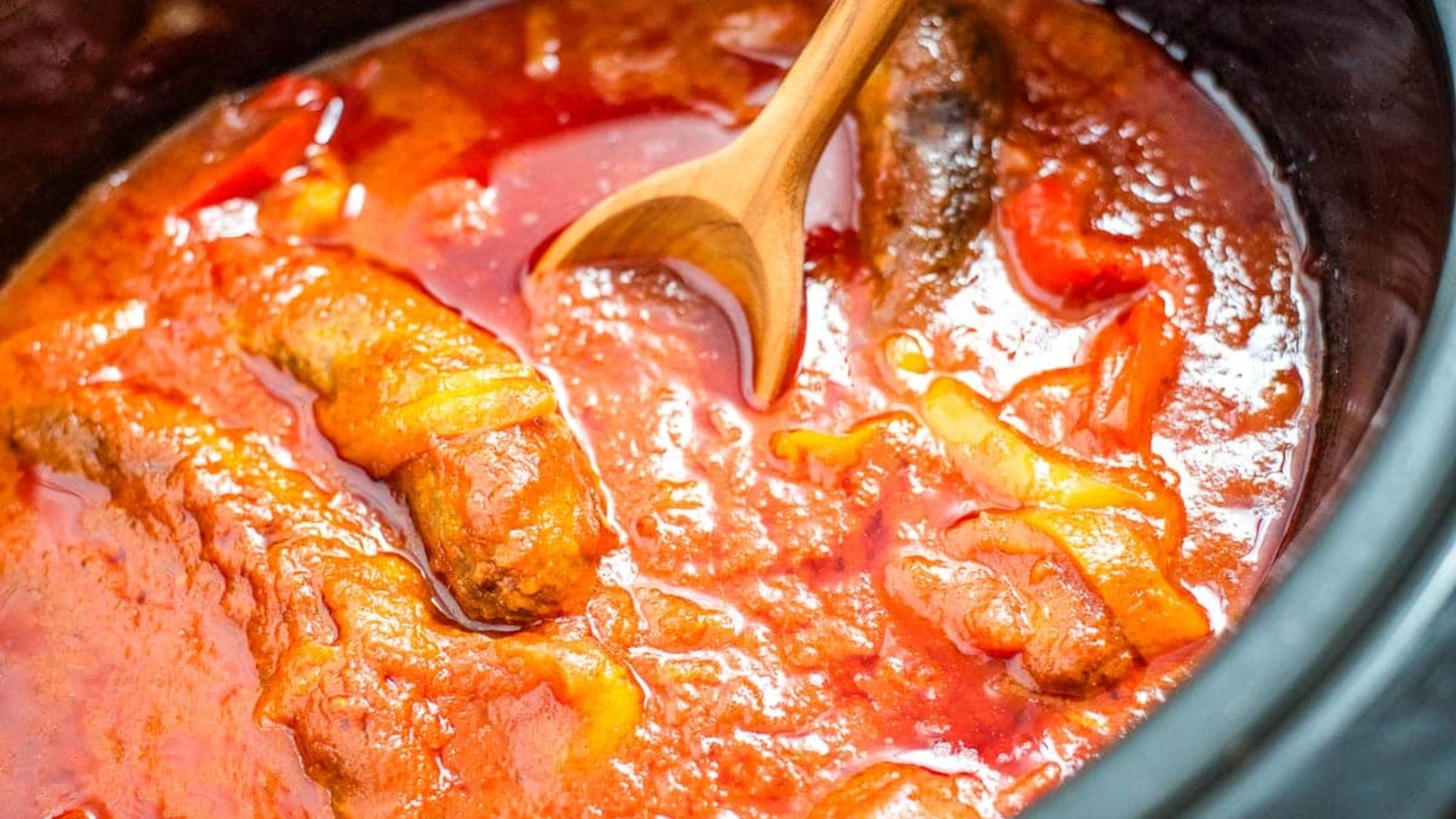 A crock pot full of sausage, peppers, and marinara sauce.