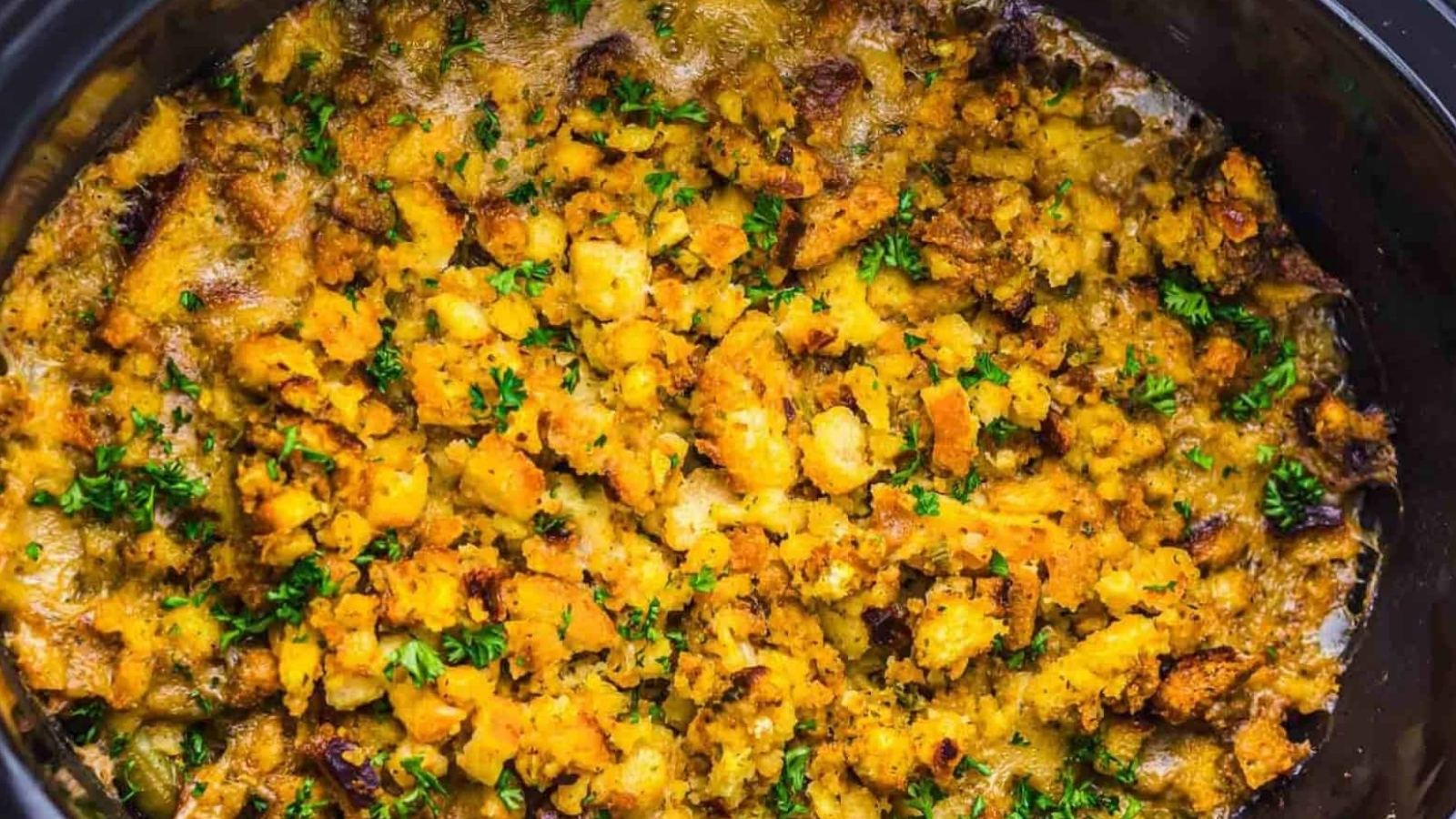 Golden-brown stuffing topped with chopped herbs, baked until crispy in a black dish.