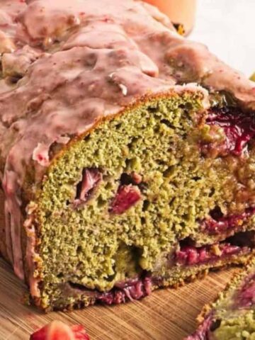 Sliced loaf of strawberry banana bread on a wooden board, surrounded by fresh strawberries and bananas.