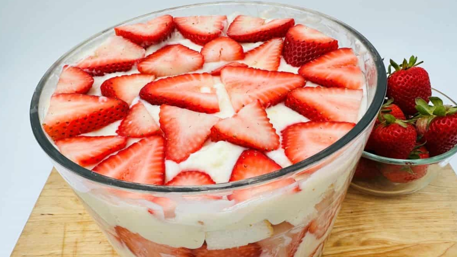 A bowl of strawberry trifle on a wooden surface.