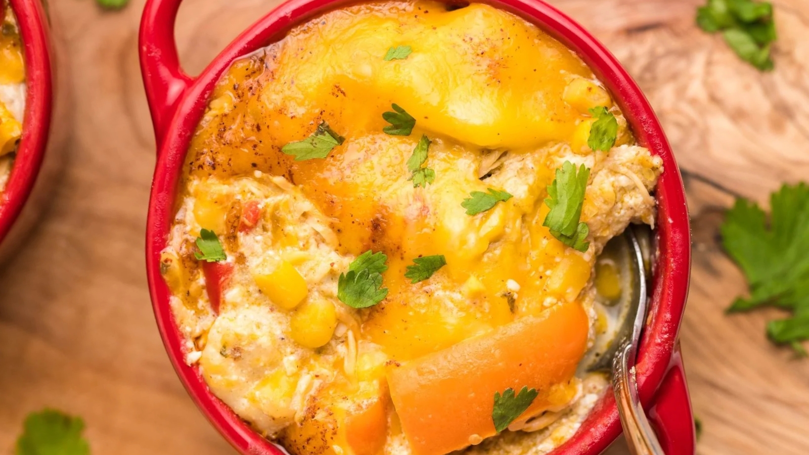 Slow cooker chicken enchilada casserole topped with melted cheese and fresh cilantro in a red bowl.