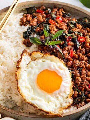 A bowl of ground pork topped with fresh basil leaves.