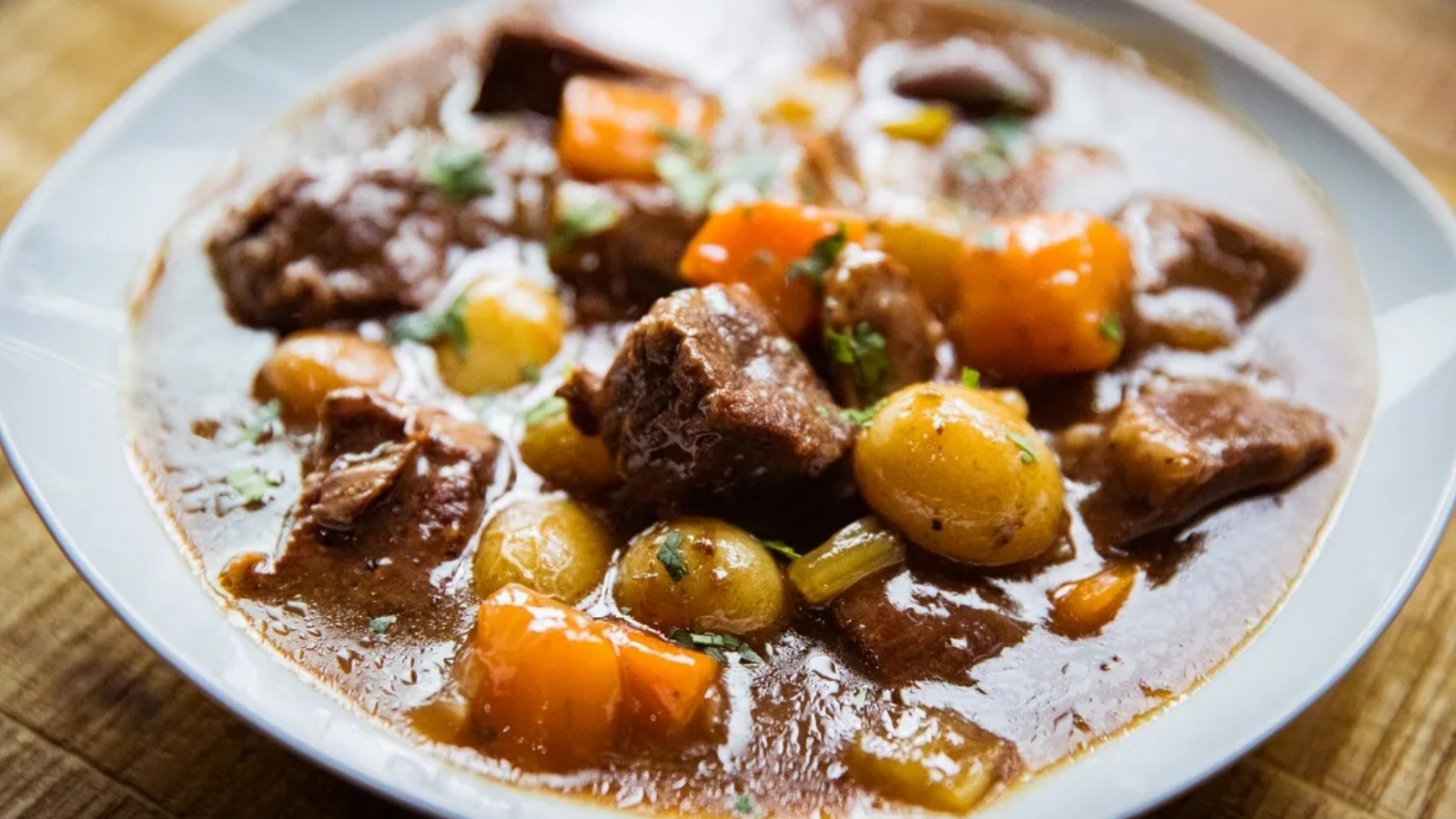 Chunks of beef, baby potatoes, carrot pieces, and celery in brown gravy served in a white bowl.