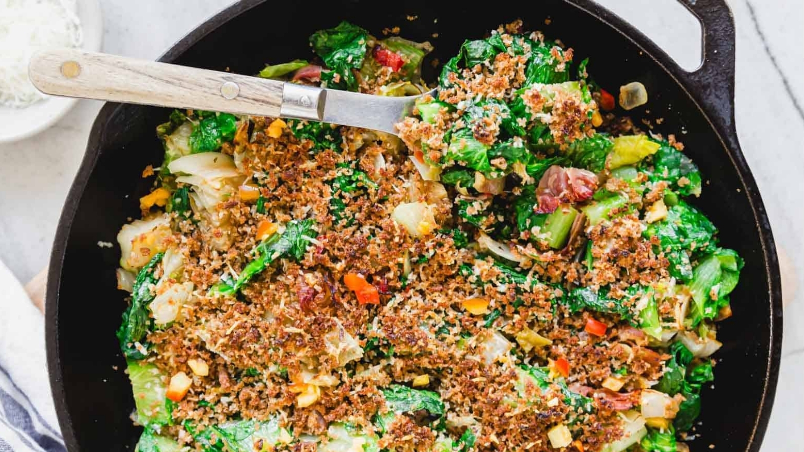 Cast iron skillet with Utica greens and wooden handle serving spoon.