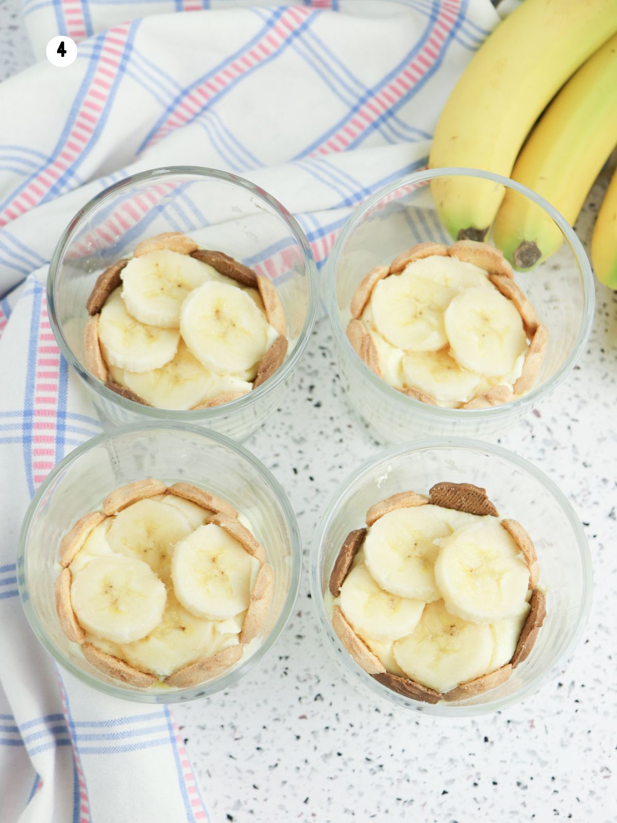 Adding sliced bananas on top of pudding and bunny grahams in individual parfait cups.
