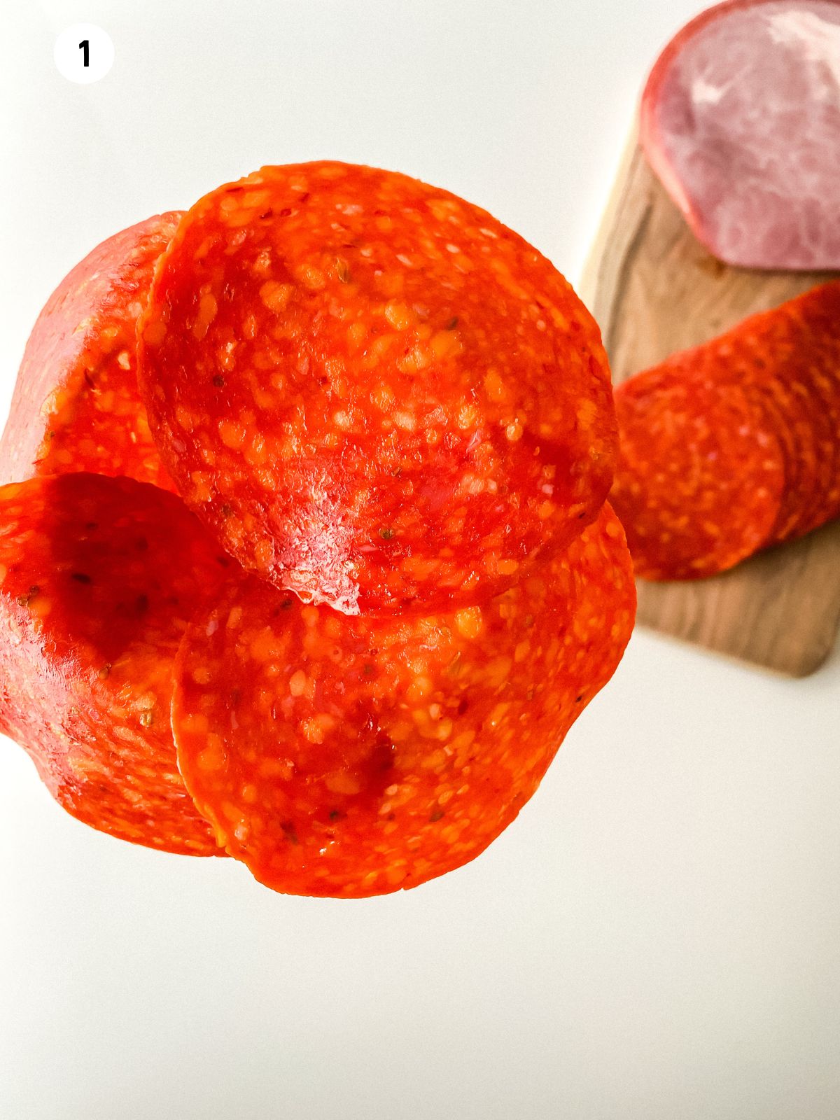 Pepperoni slices layered around the rim of a wine glass to start forming a meat rose.