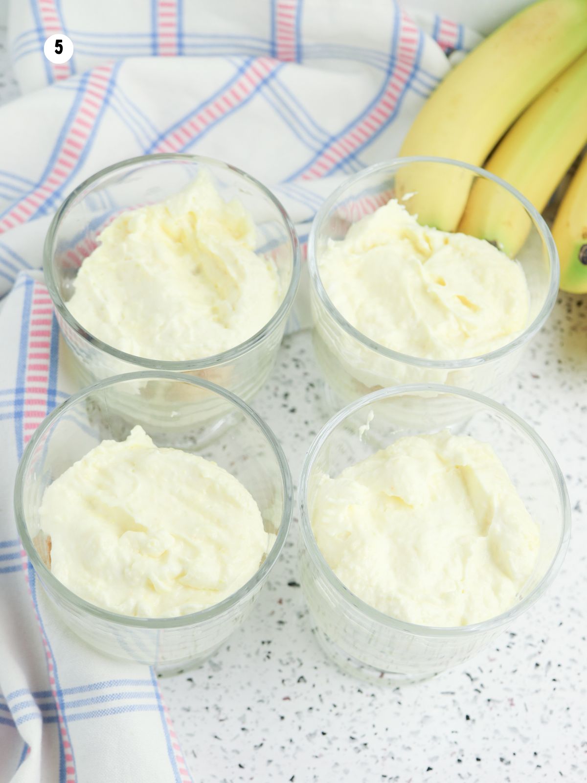 Topping banana pudding parfait cups with a final layer of vanilla pudding mixture.