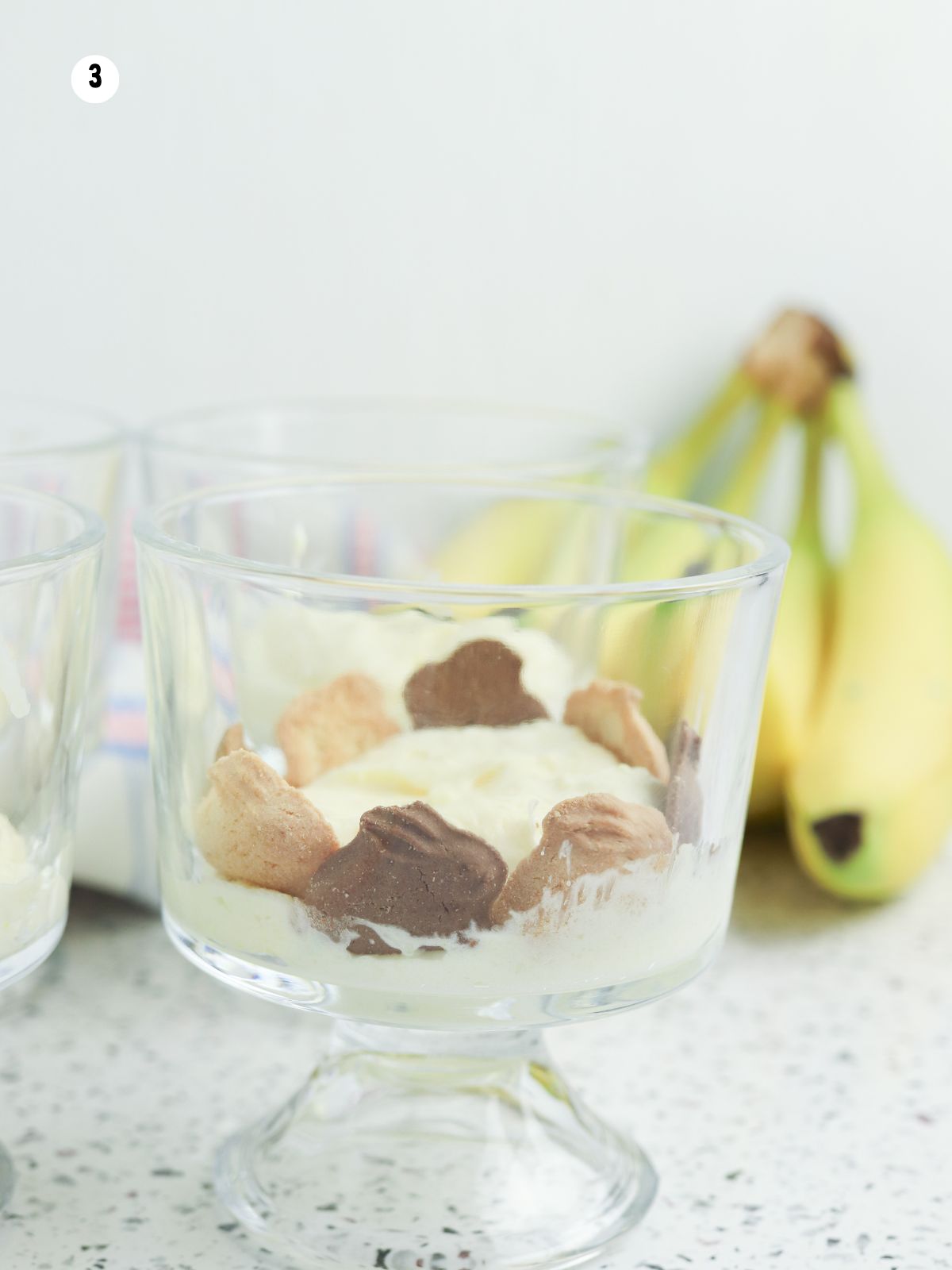 Layering bunny grahams and vanilla pudding in a glass dish to build banana pudding parfait cups.