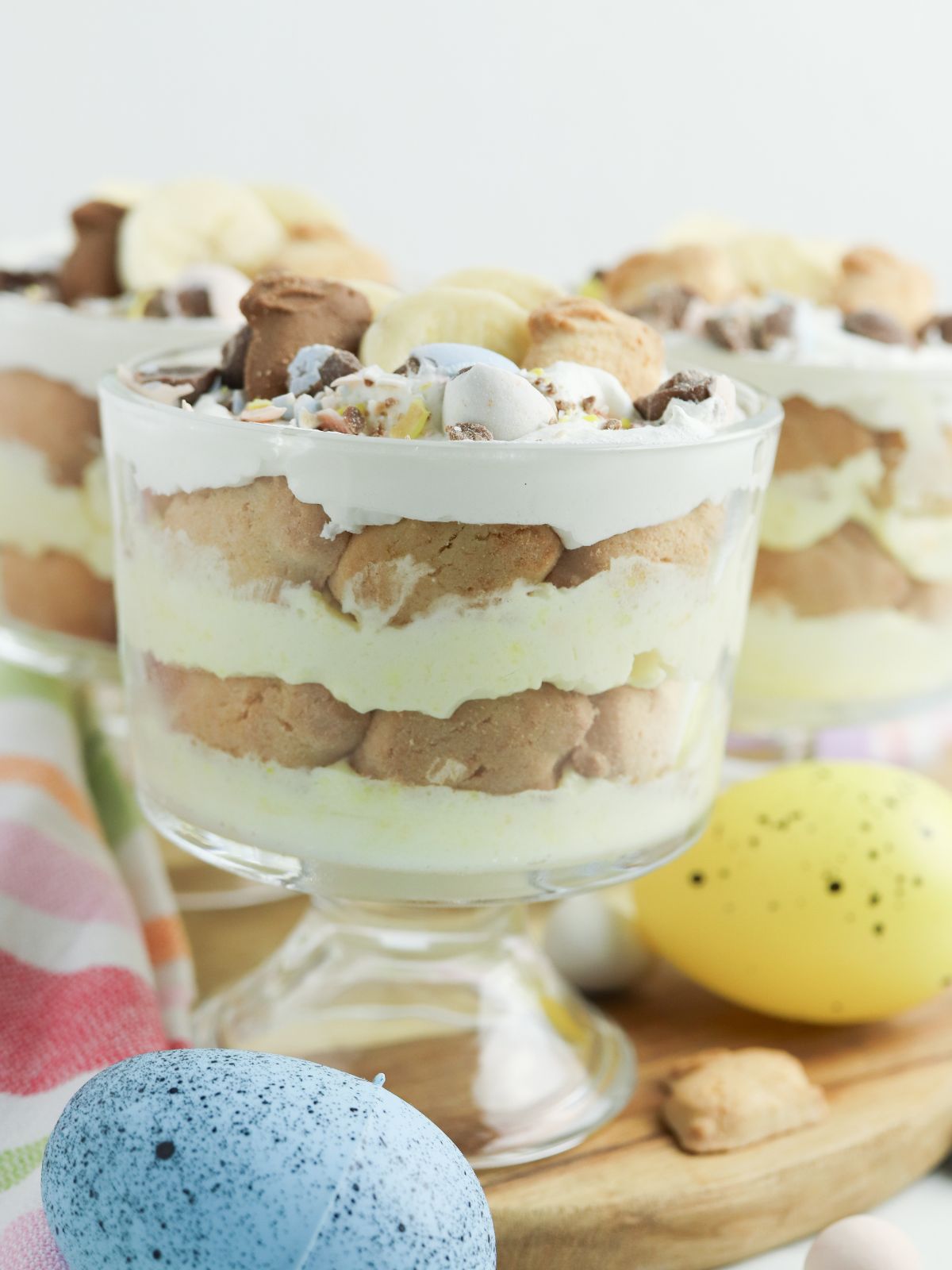 Individual Easter banana pudding parfait in a glass dish with layers of vanilla pudding, bunny grahams, sliced bananas, whipped topping, and mini chocolate eggs.