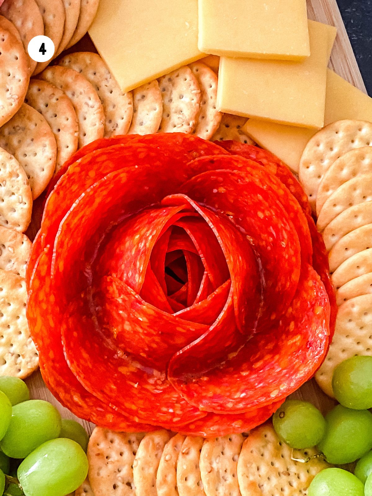 Pepperoni rose arranged in the center of a charcuterie board with crackers and cheese.
