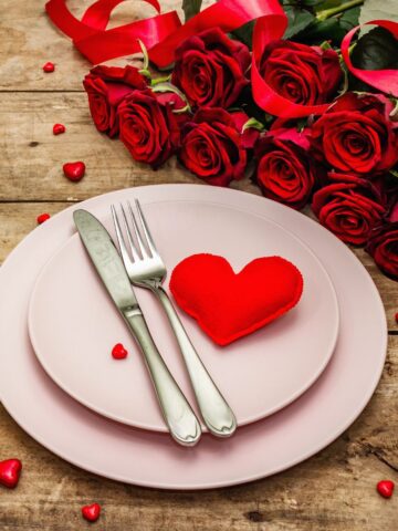 pink dishes on wooden table set for Valentine's Day with hearts and roses.