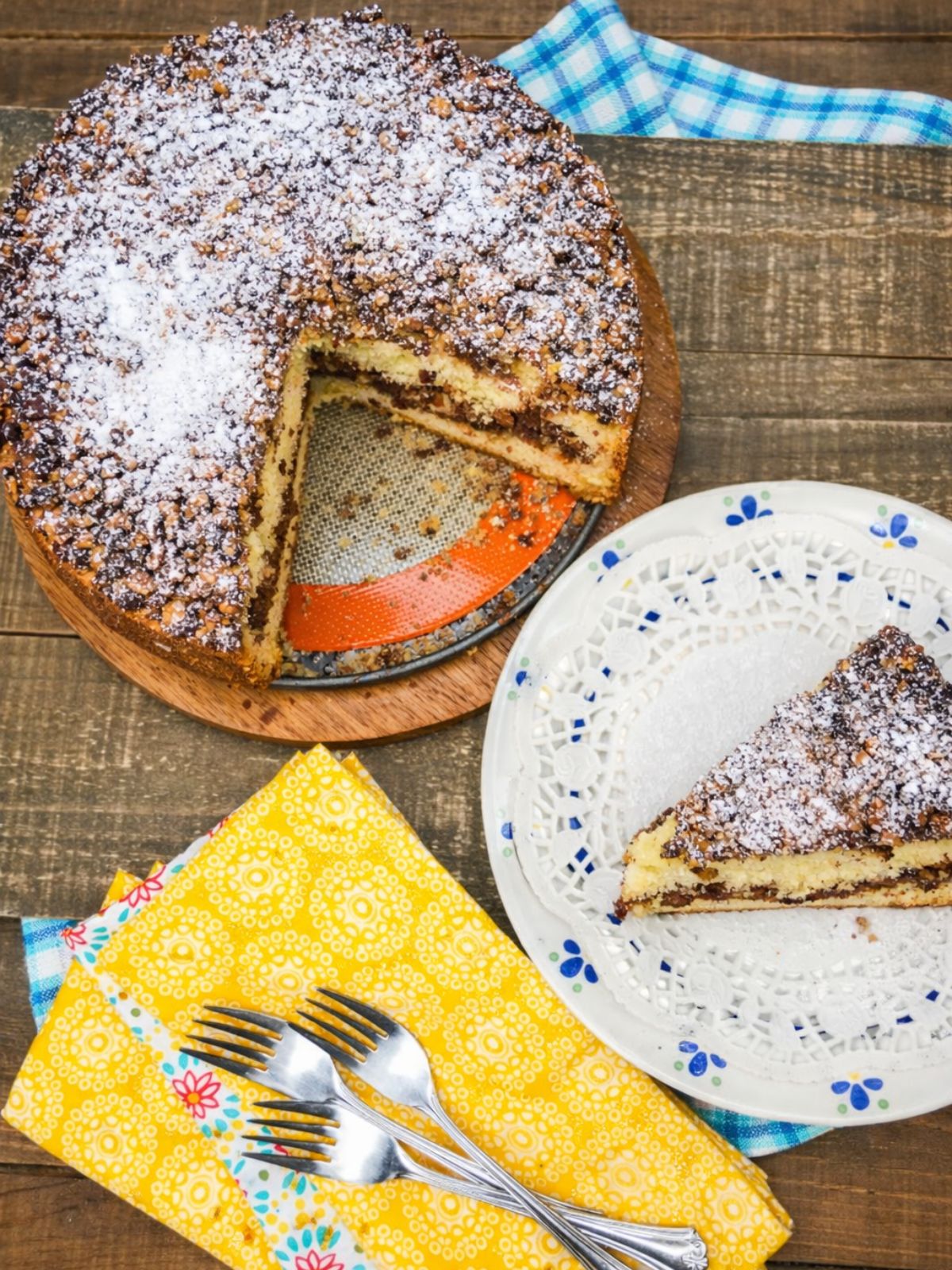Overhead view of cinnamon streusel coffee cake dusted with powdered sugar, showing a sliced piece on a serving plate.