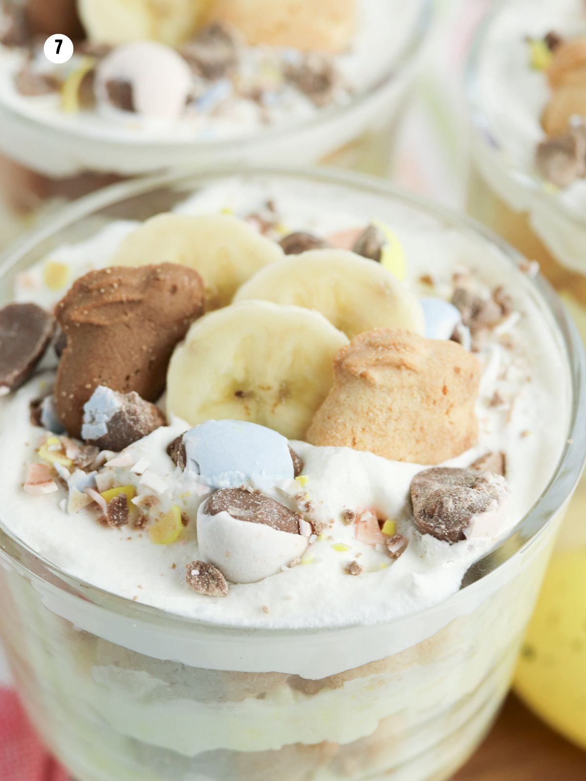 Topping banana pudding parfait with bunny grahams, mini chocolate eggs, and sliced bananas.