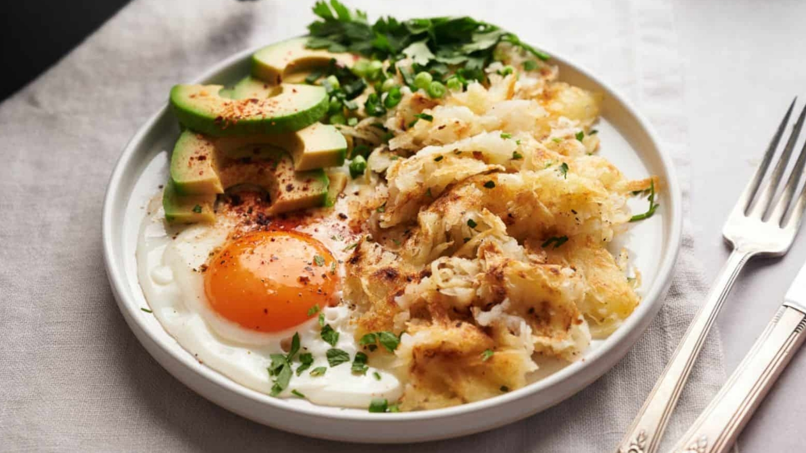 A plate with hash browns, eggs and avocado on a table.