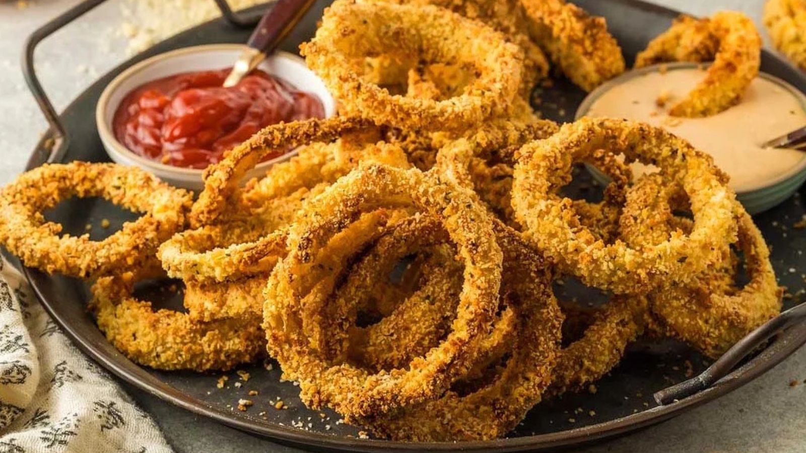 Golden-brown onion rings arranged in a bowl with a small dish of dipping sauce.