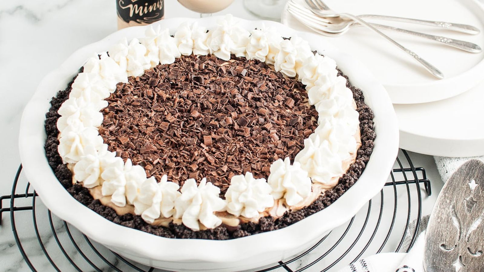 Chocolate pie topped with whipped cream and chocolate shavings in a white dish on a cooling rack.