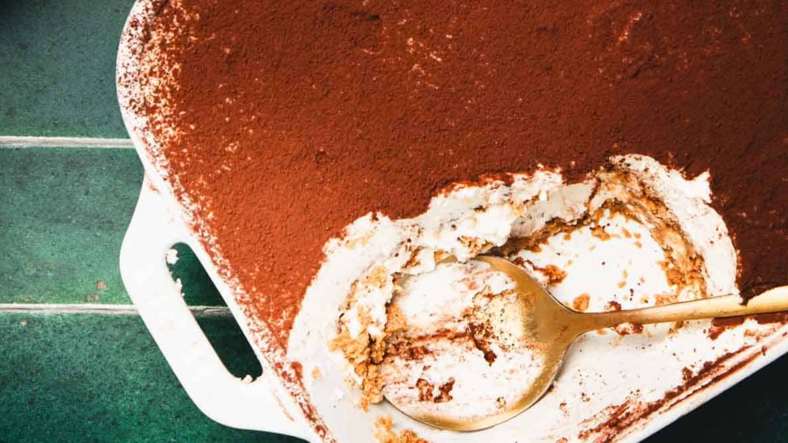 A slice of tiramisu dessert topped with cocoa powder on a plate with a gold-colored fork.