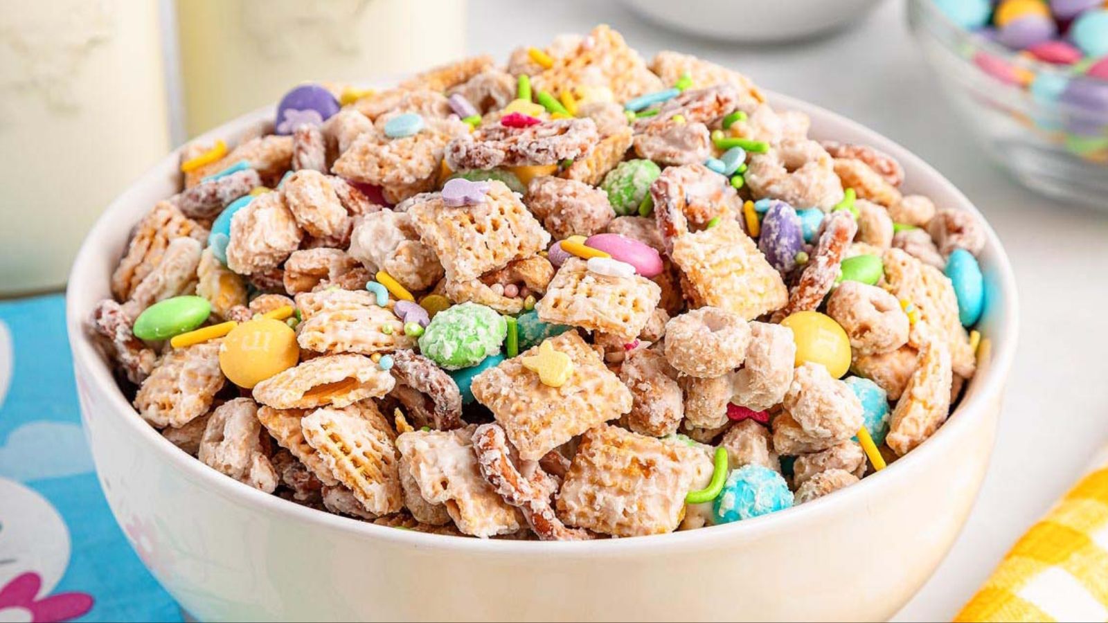 A mix of popcorn, pretzels, cereal squares, pastel candy-coated chocolates, and small marshmallows piled together.
