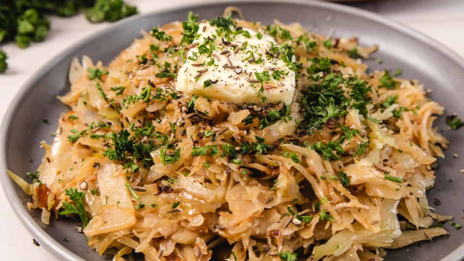 Shredded sautéed cabbage with herbs and a pat of butter on top, served on a gray plate.