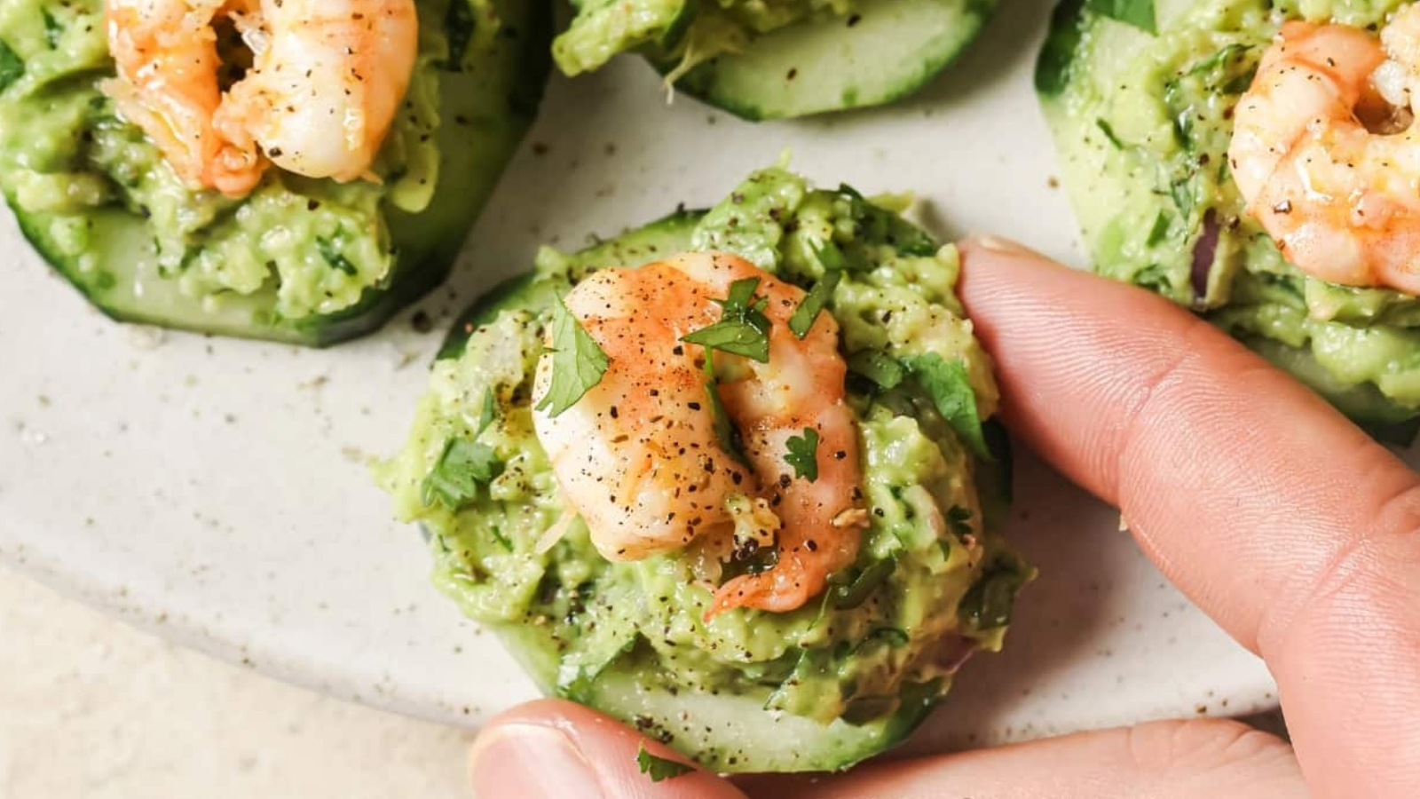 A person holding a cucumber with shrimp and guacamole.