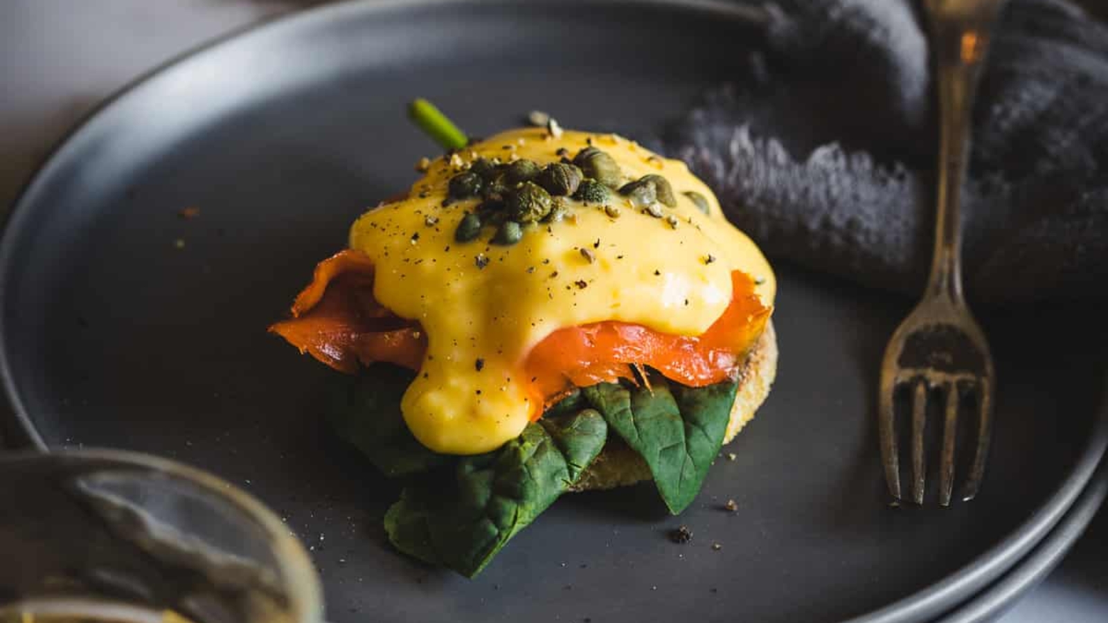 A person holding an eggs benedict with salmon and capers on a plate.