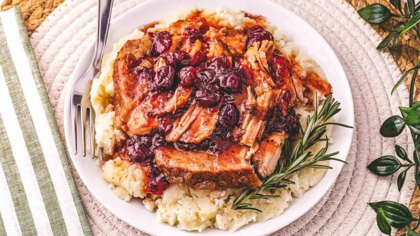Shredded pork with cranberry sauce served over mashed potatoes, garnished with rosemary on a white plate.