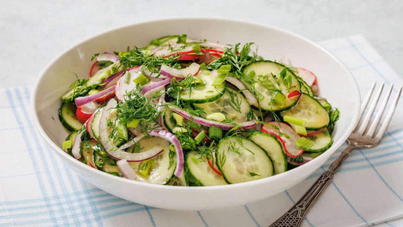 Bowl of Radish Salad with red onion, radishes, and fresh herbs on a plaid cloth, accompanied by a fork.
