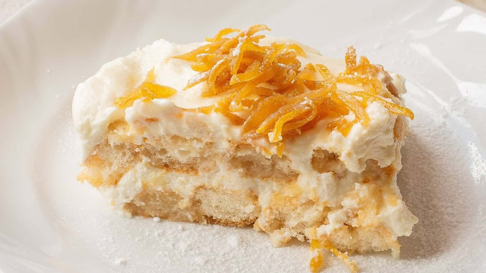 A slice of creamy tiramisu topped with shredded orange zest on a white plate.