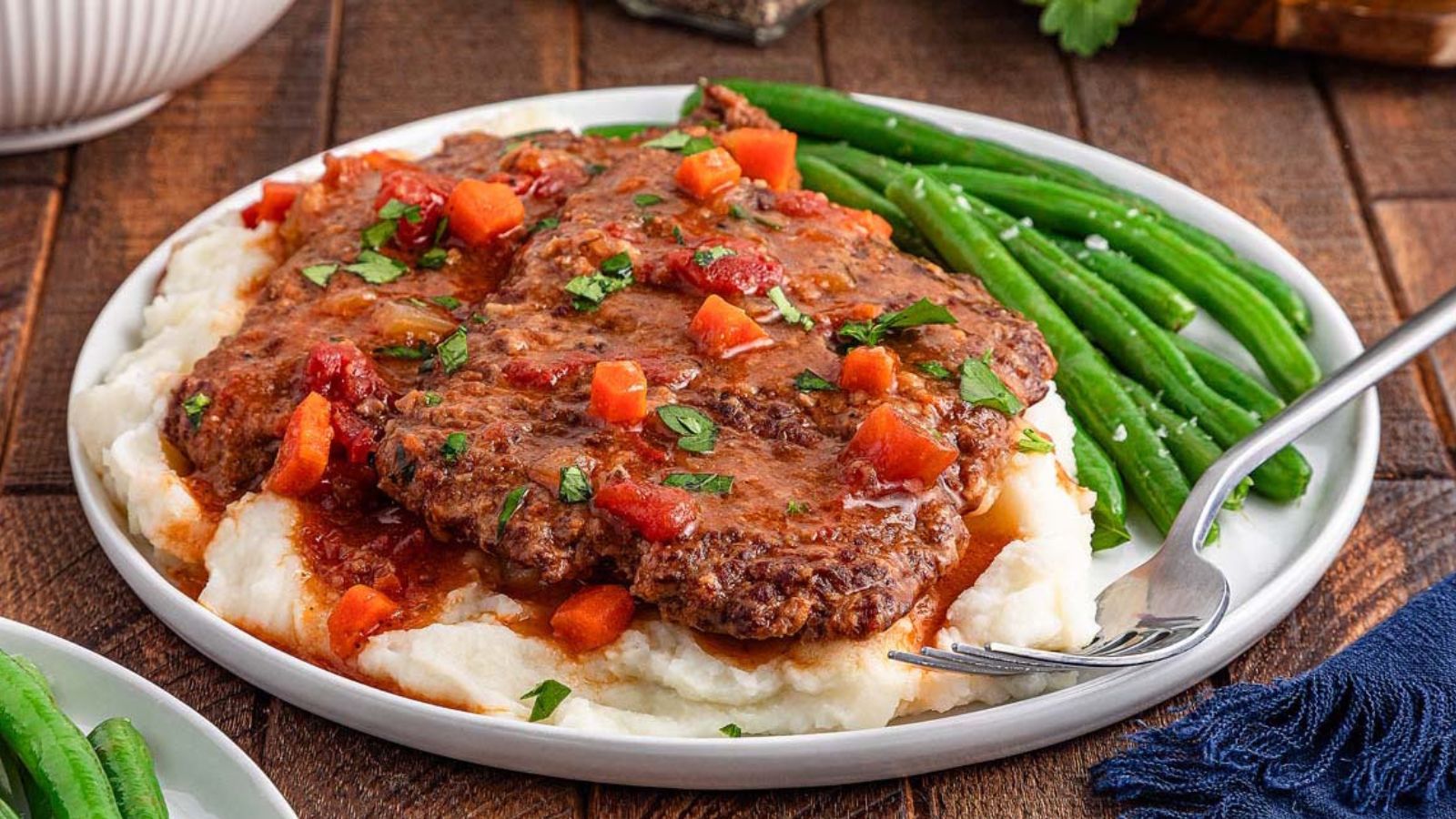 Braised beef steak covered in thick tomato-based gravy with visible chopped onions on a plate.