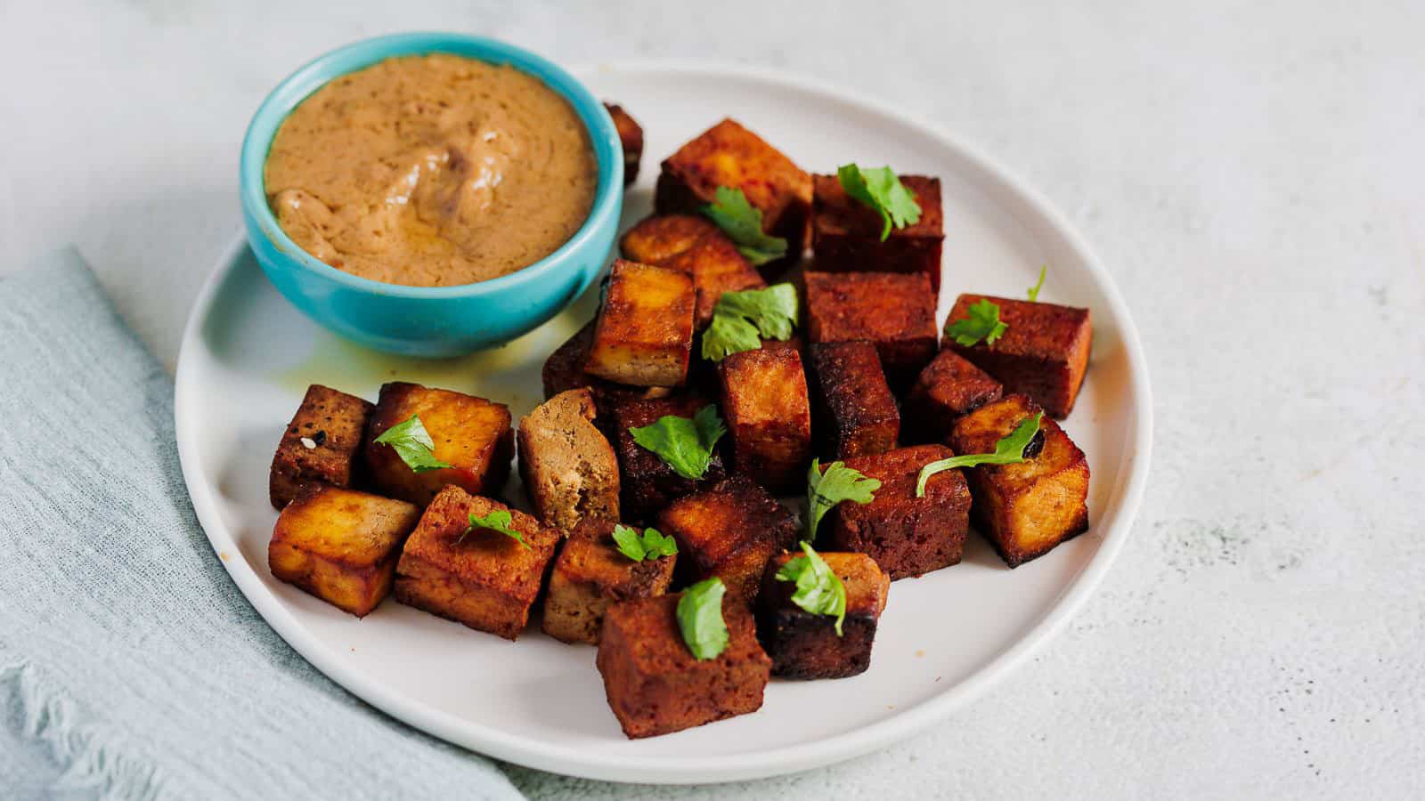 A fried marinated tofu on white plate with dipping sauce.