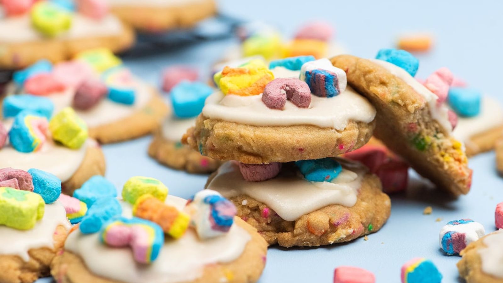 Sugar cookies topped with white icing and colorful marshmallows on a light blue surface.