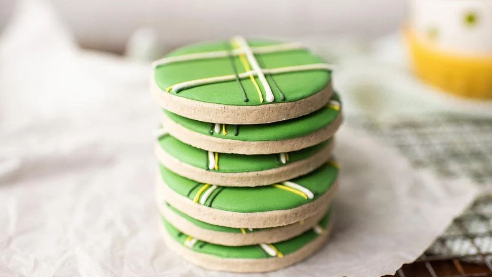 A stack of round sugar cookies with green icing and white and yellow striped lines on top.