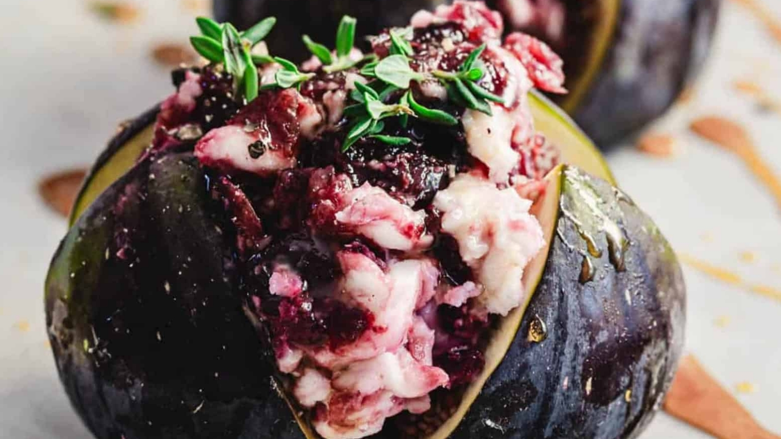 A close-up of a fig stuffed with creamy cheese, berries, and garnished with fresh thyme.