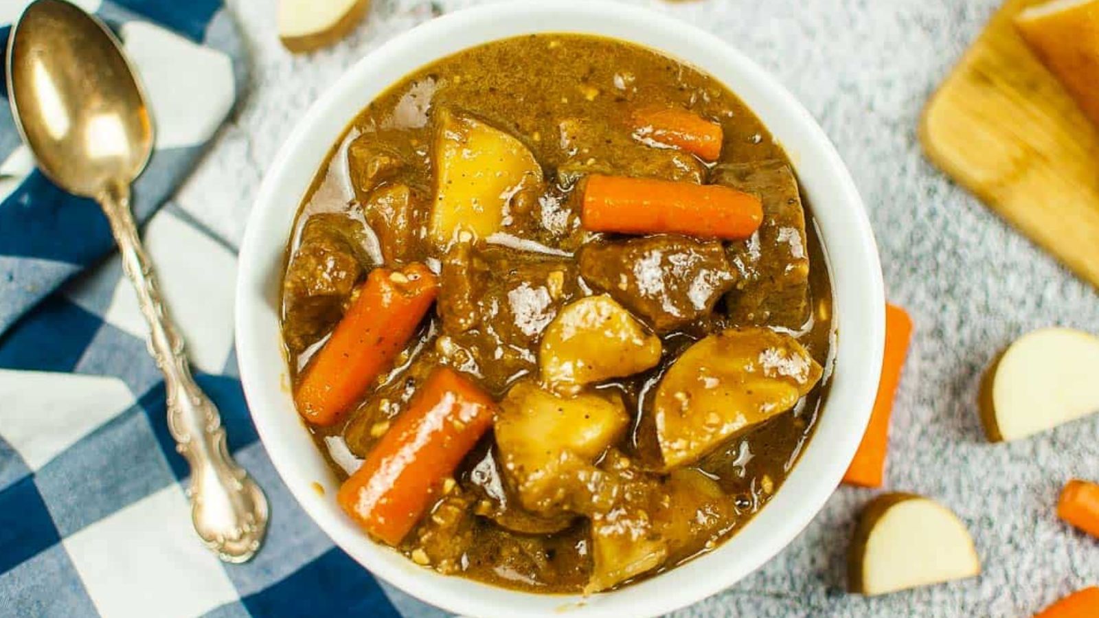 Top view of a bowl of Guinness beef stew with a black checked napkin and a spoon.