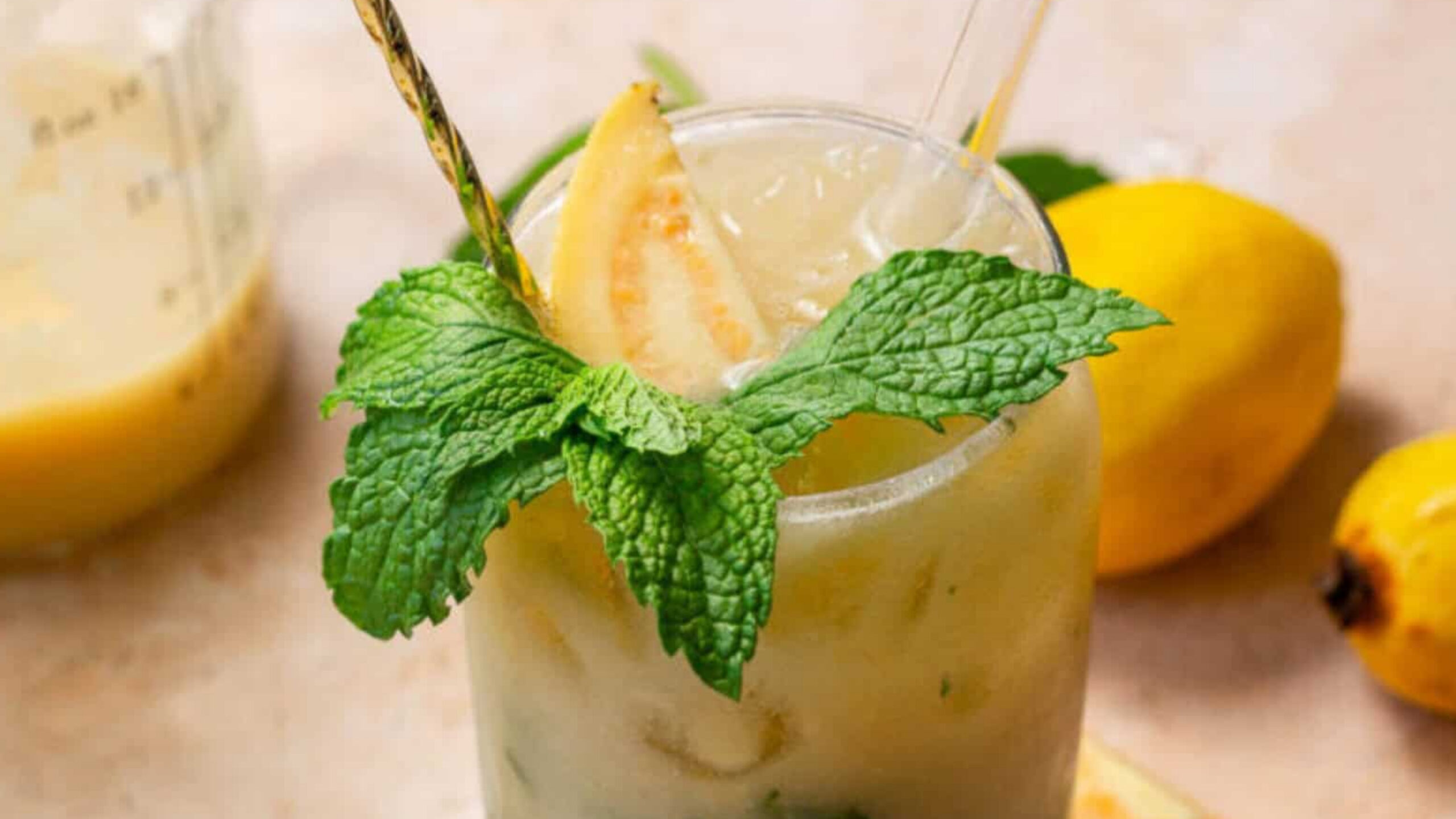 A refreshing guava lemonade garnished with mint leaves and a guava slice, with lemons in the background.