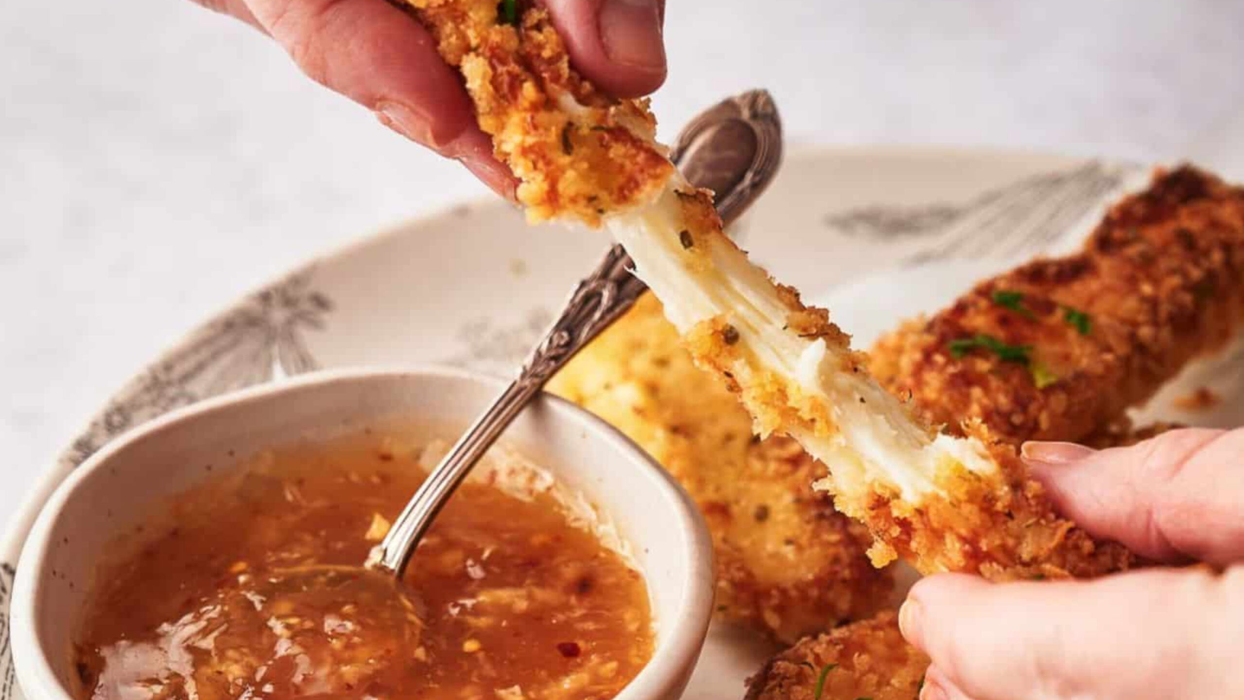 Someone pulling a mozzarella stick apart and showing the stretchy cheese.