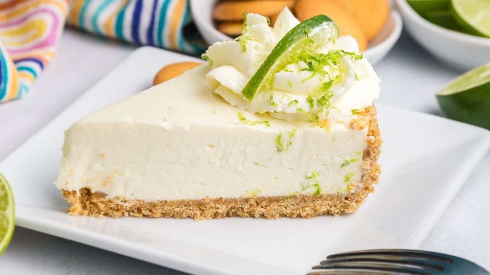 Slice of key lime cheesecake topped with whipped topping and lime slices on a plate.