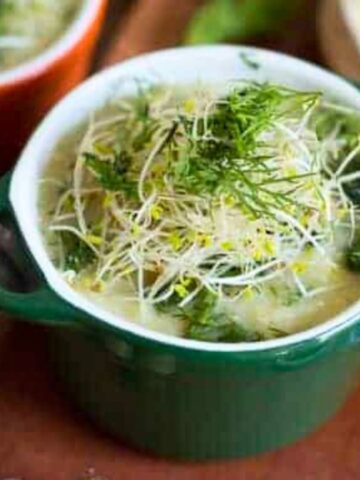 Two bowls of soup with dill on a wooden cutting board.