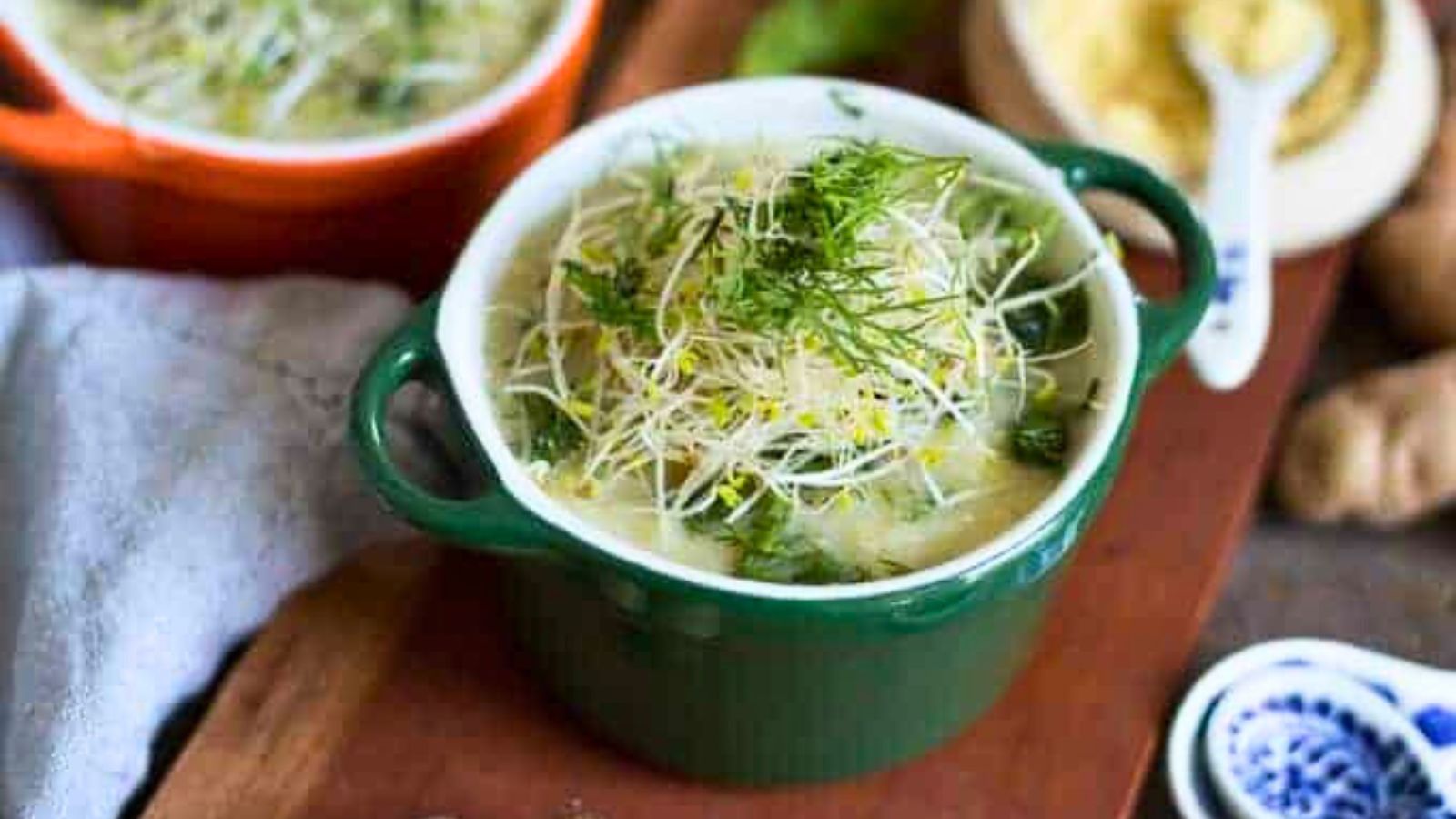 Two bowls of soup with dill on a wooden cutting board.