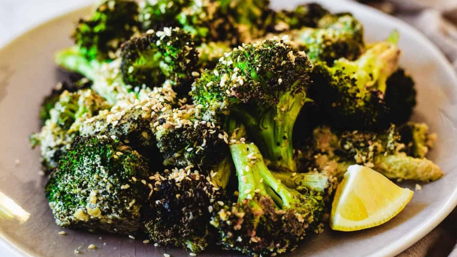 Roasted broccoli topped with sesame seeds on a plate, served with lemon wedges.