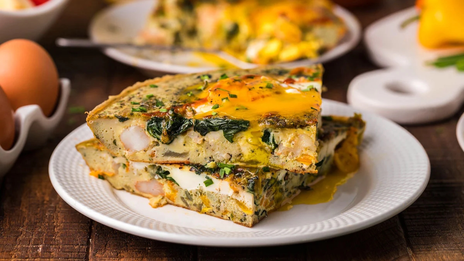 Shrimp and spinach omelette slice topped with a sunny-side egg and herbs on a white plate.