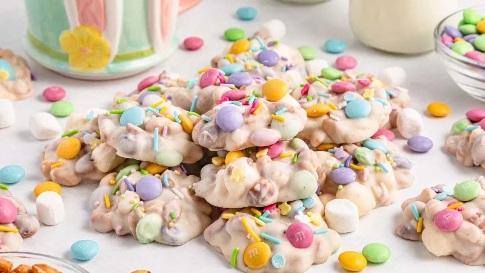 White chocolate candy clusters with pastel candies, mini marshmallows, and sprinkles arranged on a surface.