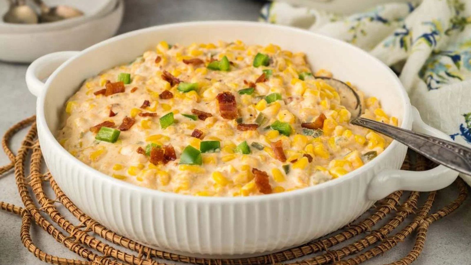A pot filled with creamy corn topped with sliced jalapeños, crumbled bacon, shredded cheese, and chopped green onions.