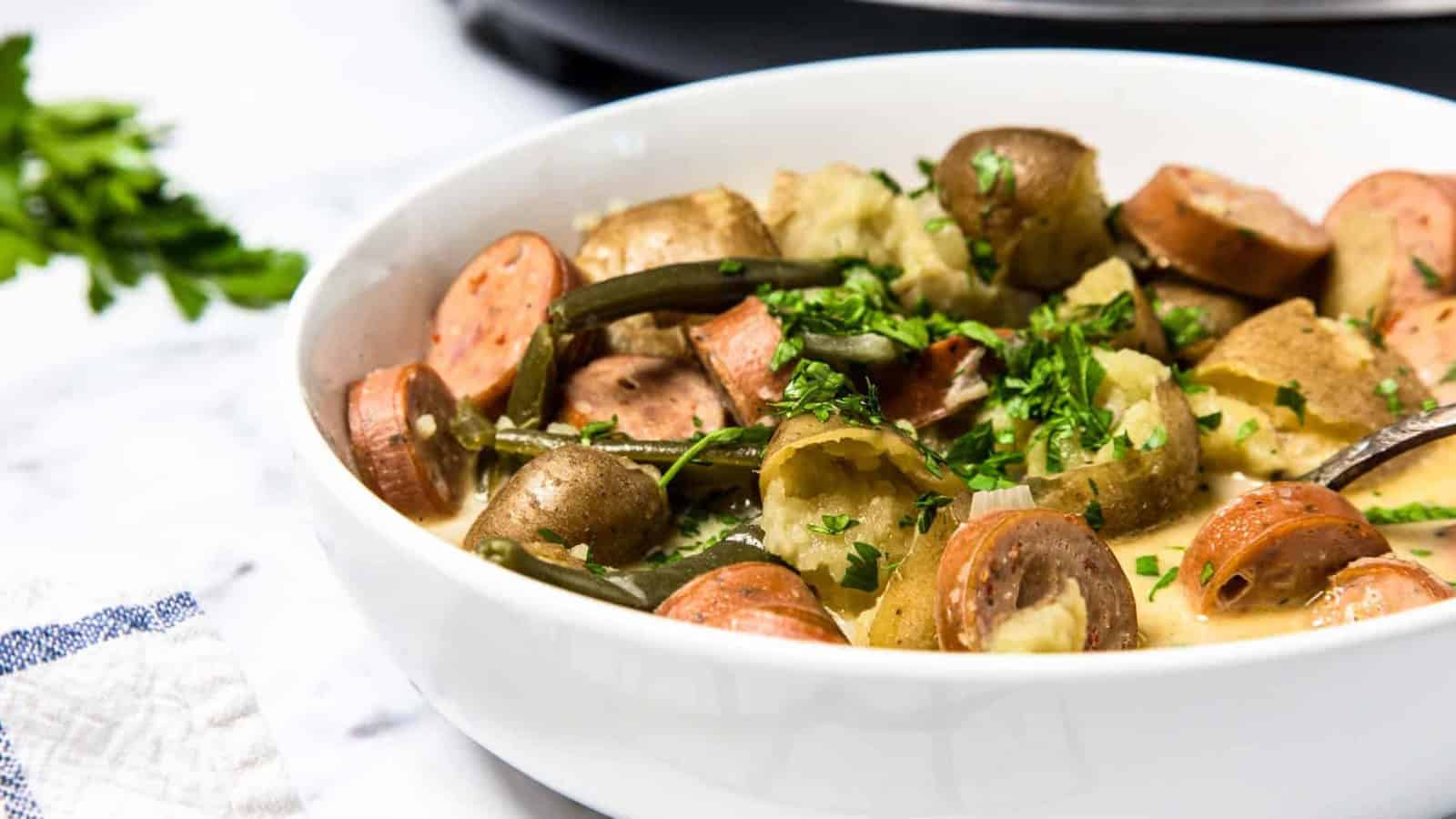 A bowl of sausage, potatoes, and green beans garnished with chopped parsley.