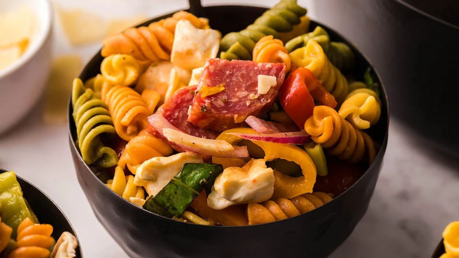 A bowl of pasta salad with sliced vegetables and herbs mixed throughout.